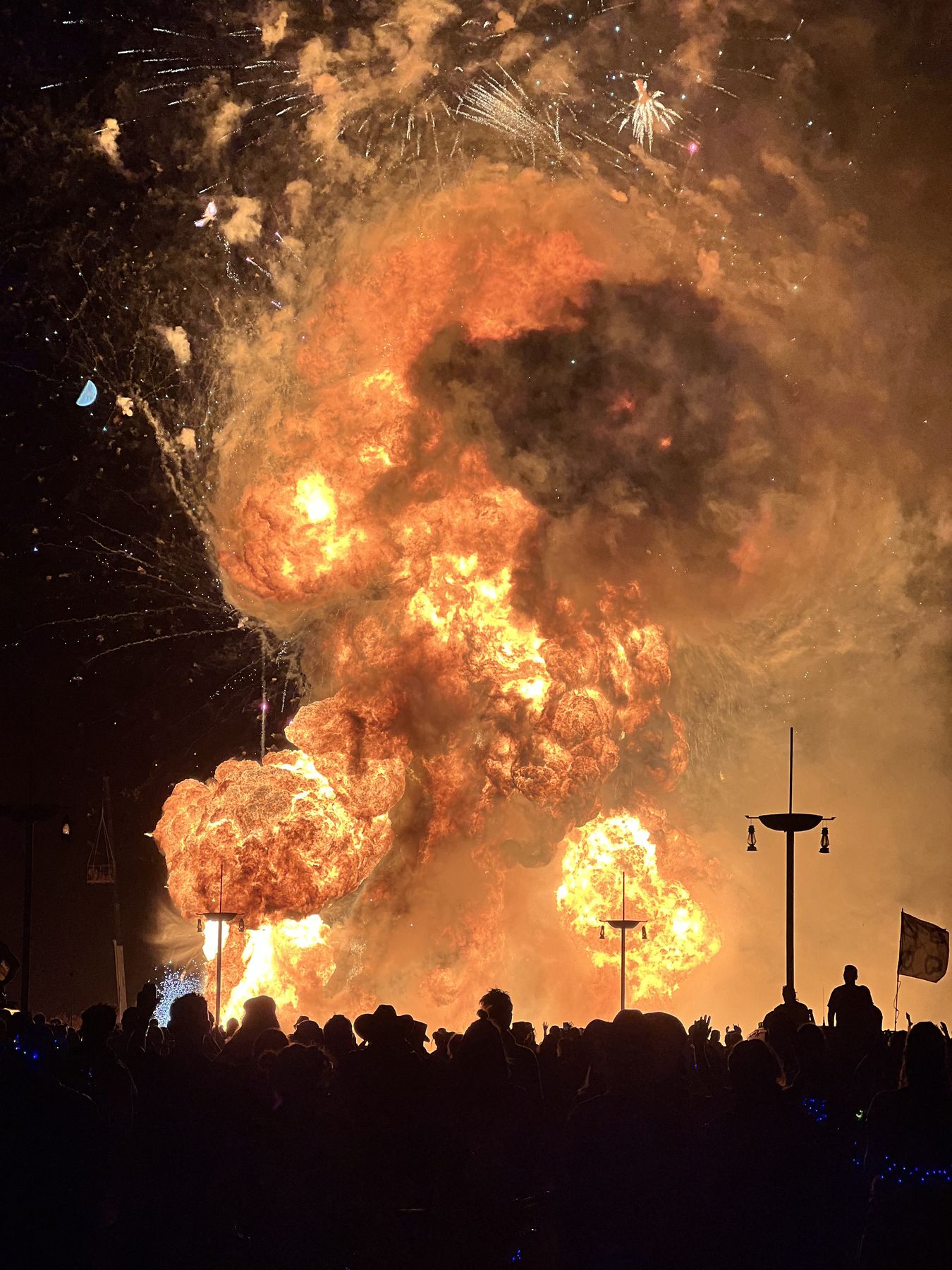 A towering wall of fire above a silhouetted crowd